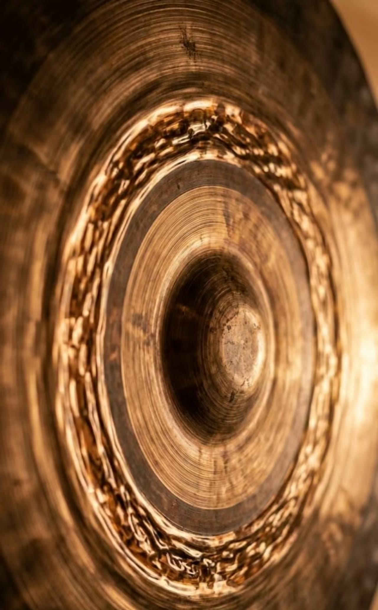 Macro detail of burnished gong metal in warm temple-red light